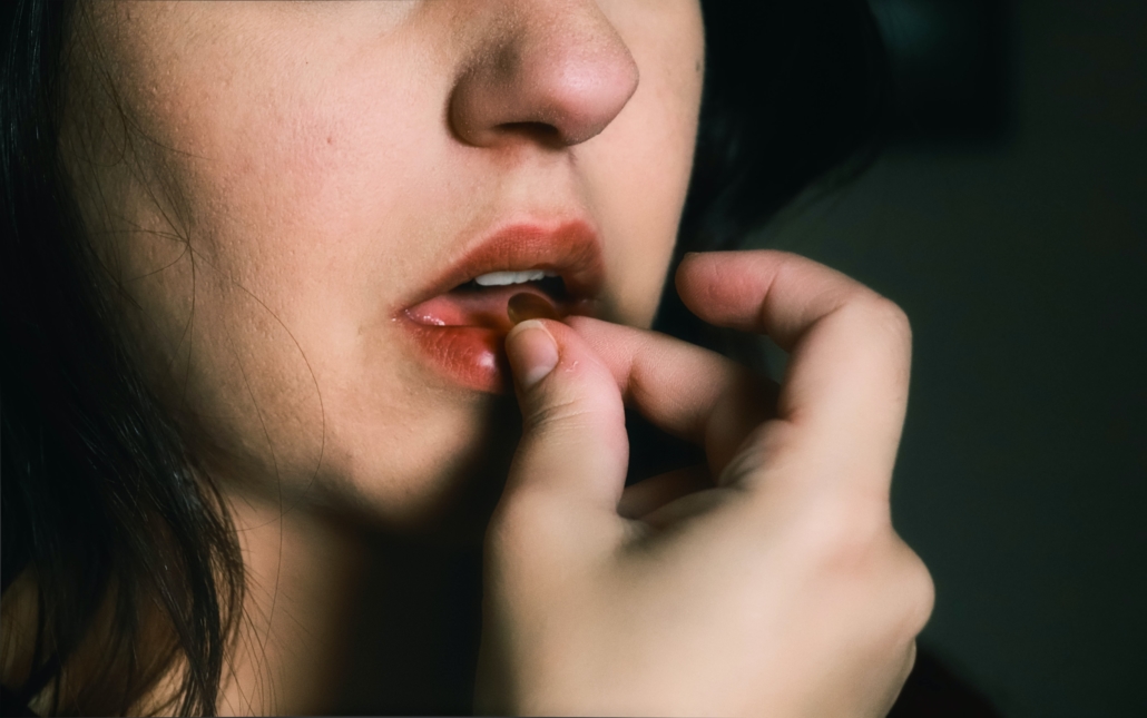 woman with red lipstick holding a pill to her lips